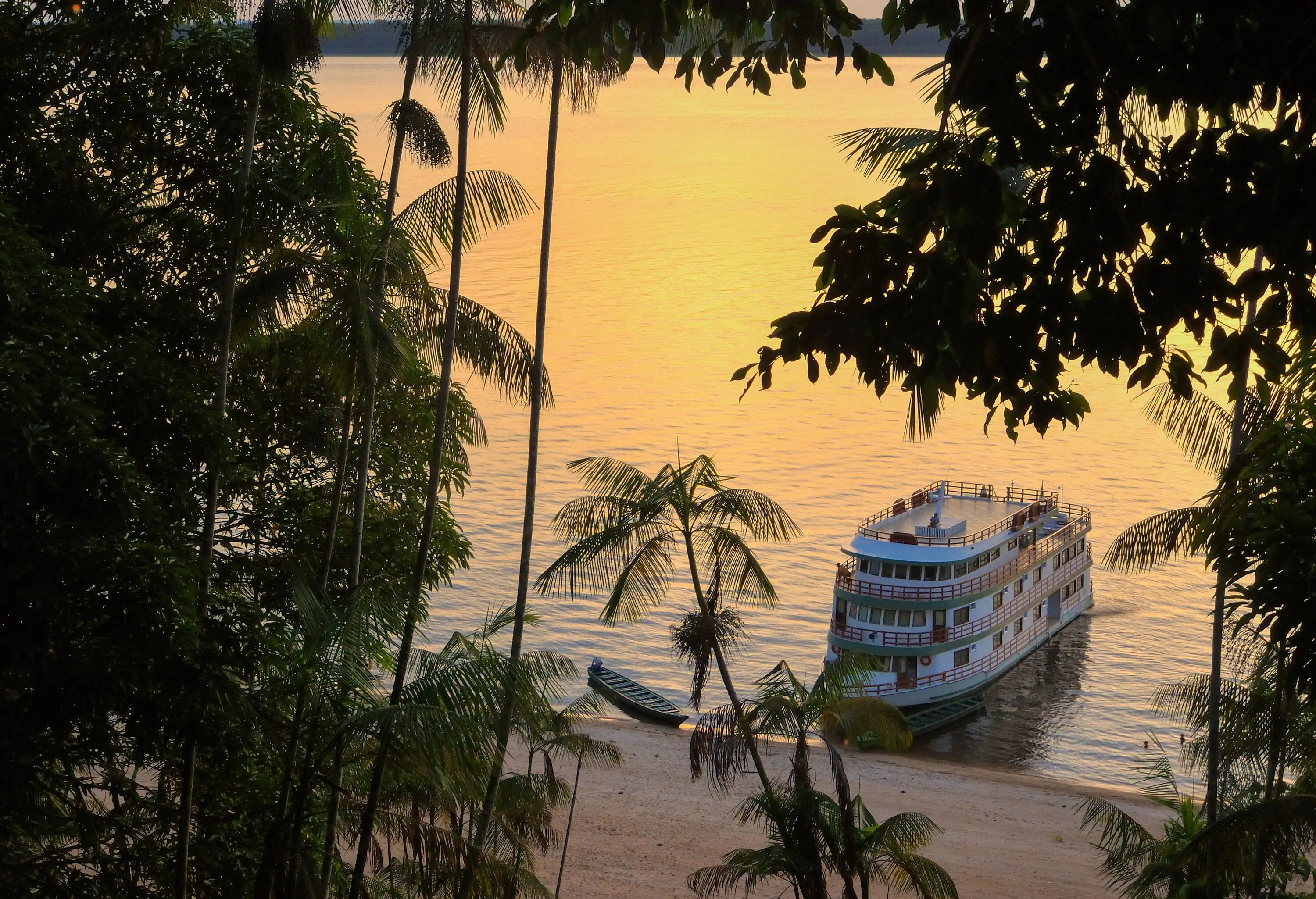 A cruise ship on the shore of a river at sunset.