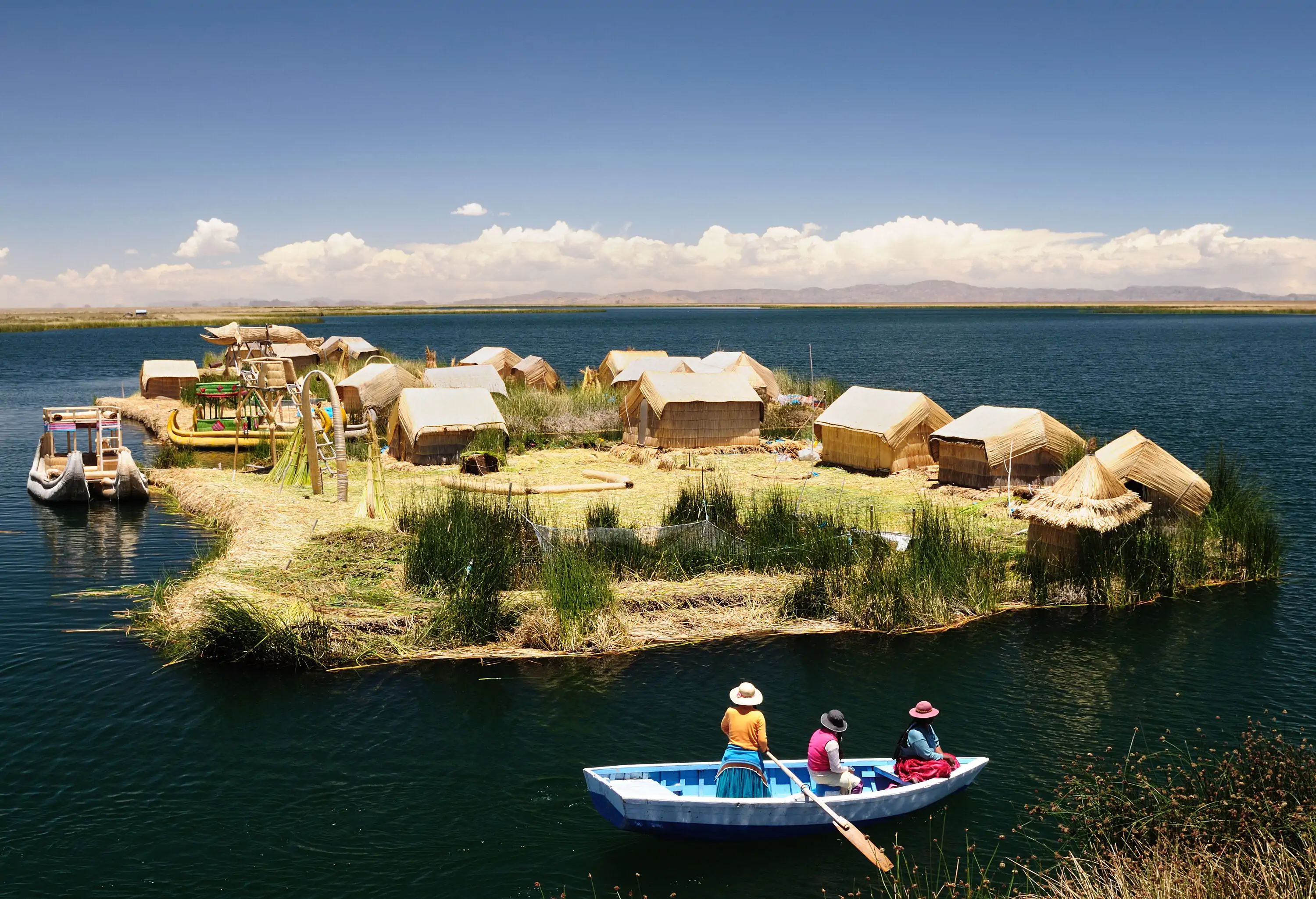 Three passersby on a boat look at the reed houses on the small island surrounded by calm waters.